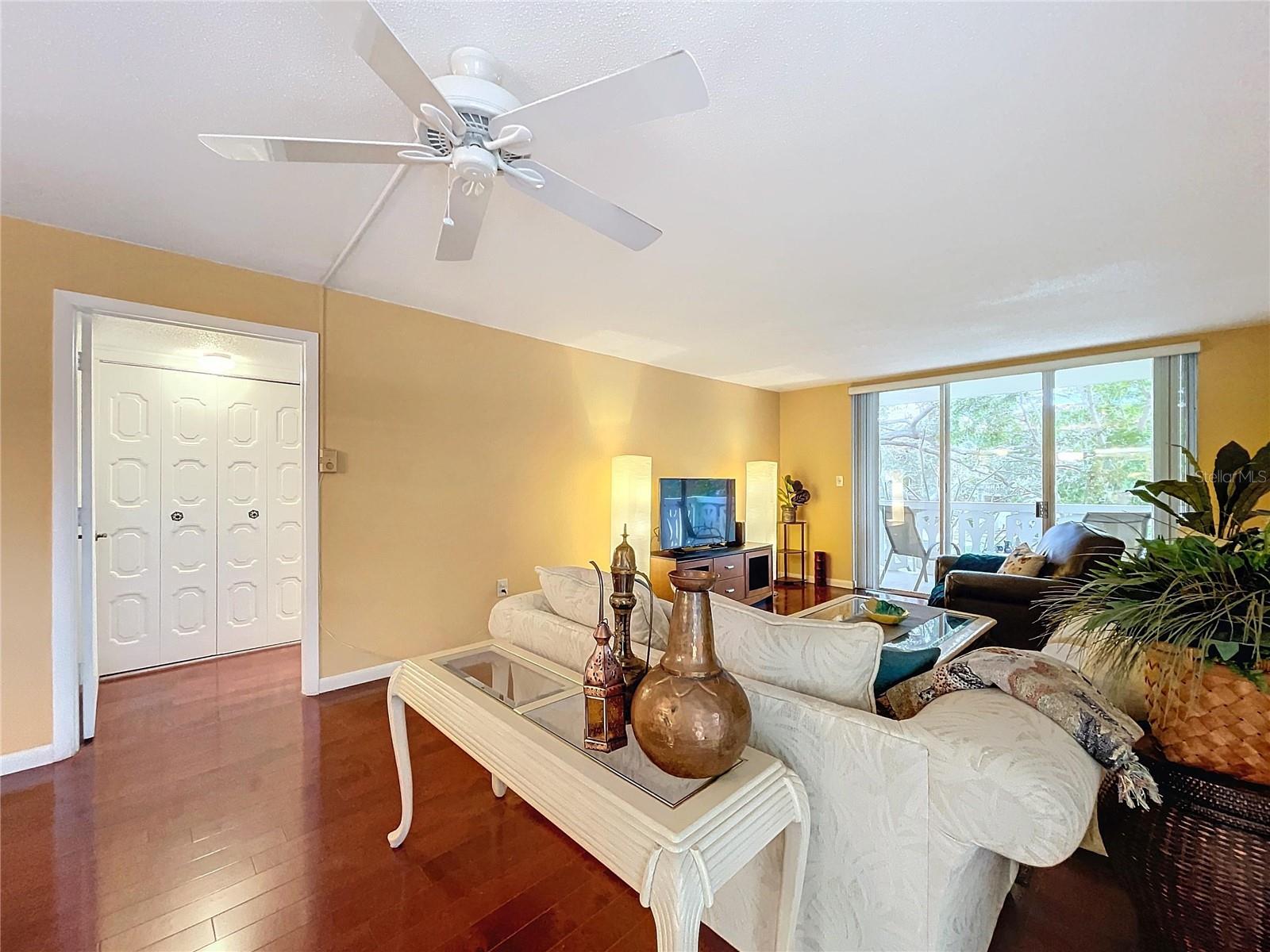 Bright and spacious living area with warm-toned walls, rich hardwood flooring, and sliding glass doors that open to the balcony for seamless indoor-outdoor living.