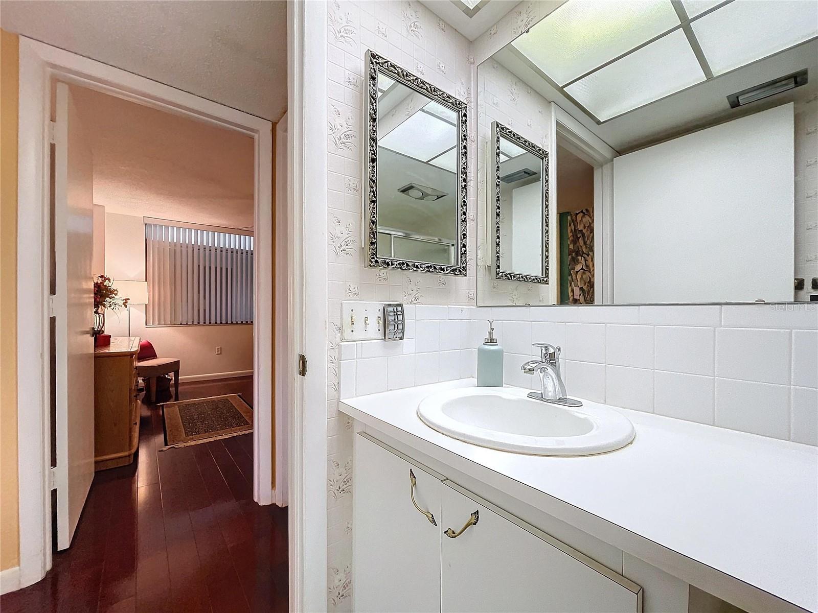 Spacious countertop and dual framed mirrors provide everyday convenience, with sightlines leading back toward the bedroom.