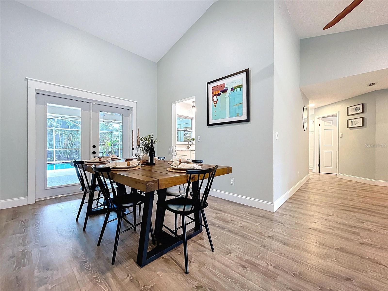 Bright and airy dining room with vaulted ceiling, stylish pendant lighting, and French doors offering views of the pool and backyard.