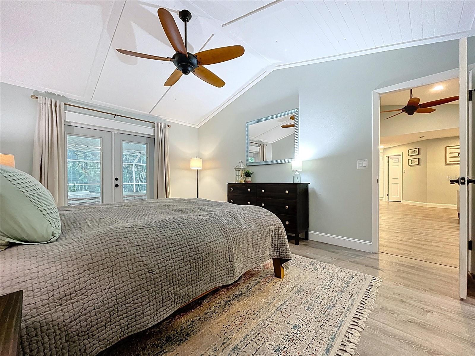 Spacious bedroom with serene wall tones, stylish furnishings, and a view into the main living area.