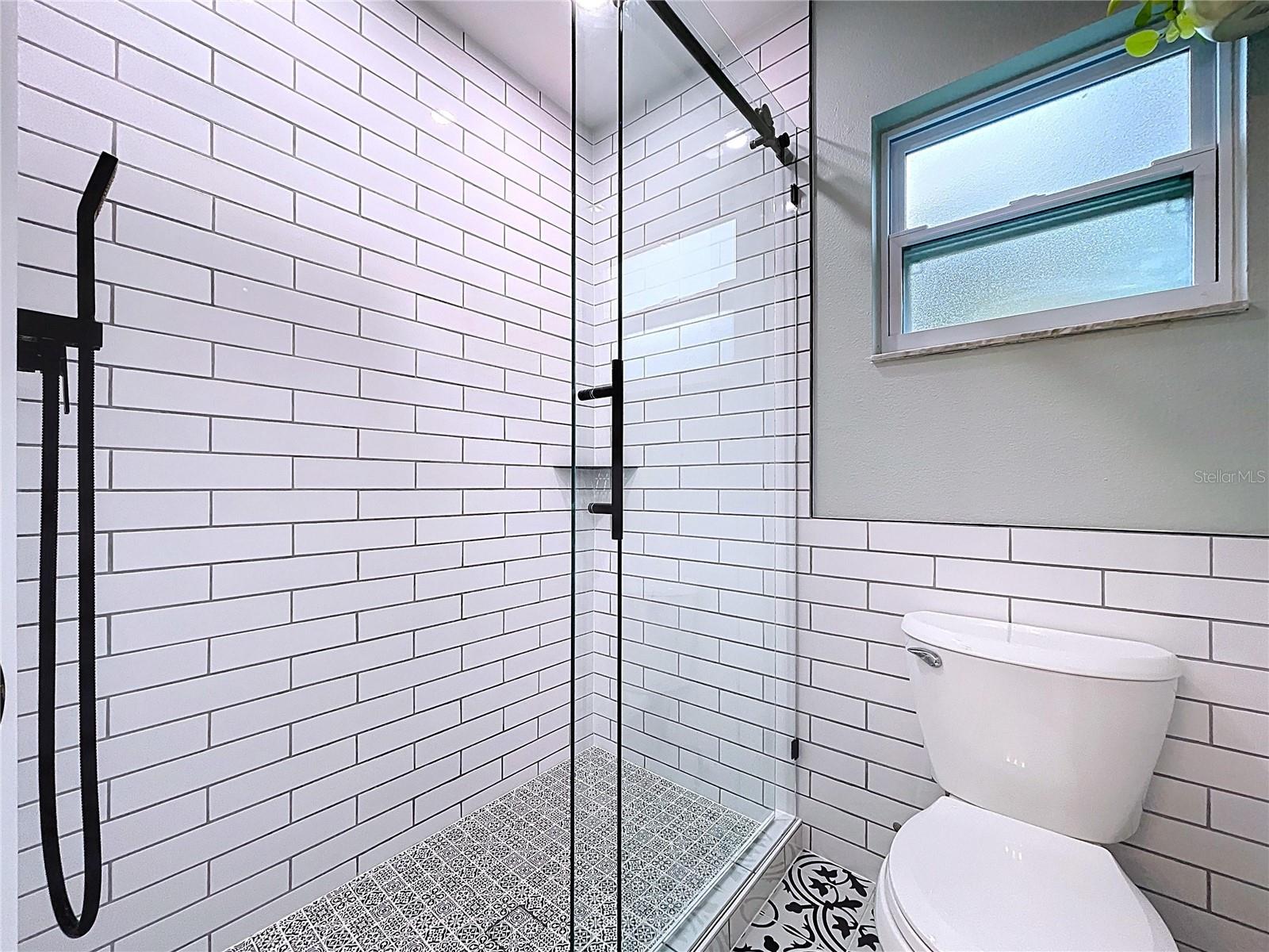 Spa-like walk-in shower with floor-to-ceiling subway tile, matte black hardware, and patterned tile flooring for a bold finish.