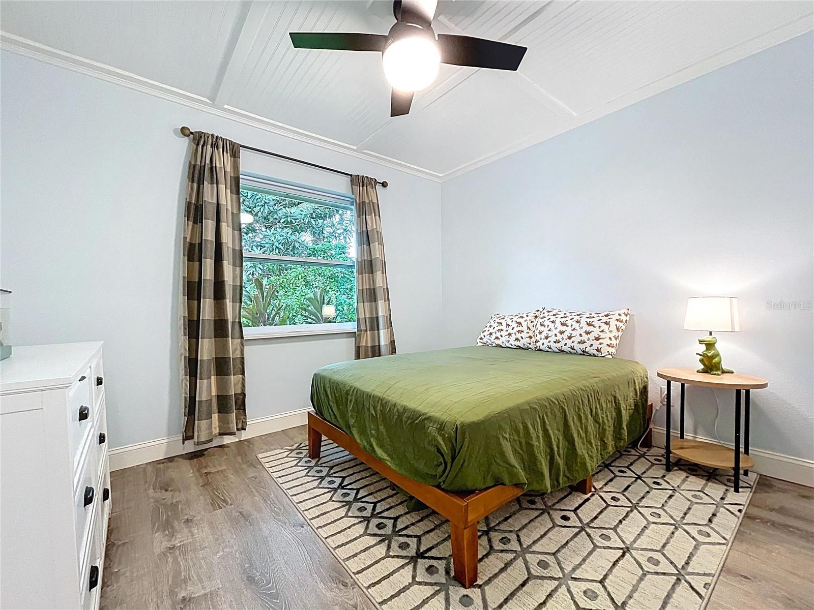 Light and bright guest room with vaulted beadboard ceiling, a large window with lush views, and wood-look flooring for a warm finish.