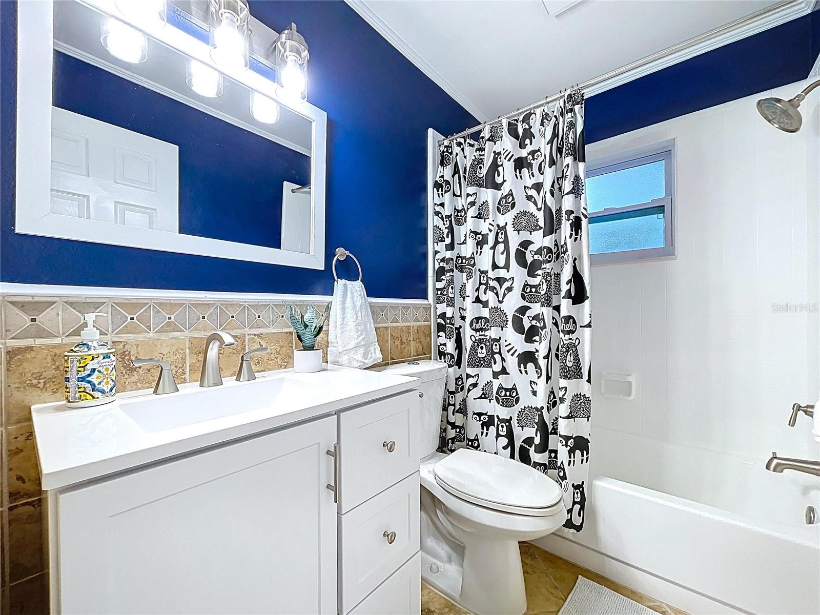 Crisp and functional full bath with a shower/tub combo, bold navy walls, and whimsical black-and-white curtain.