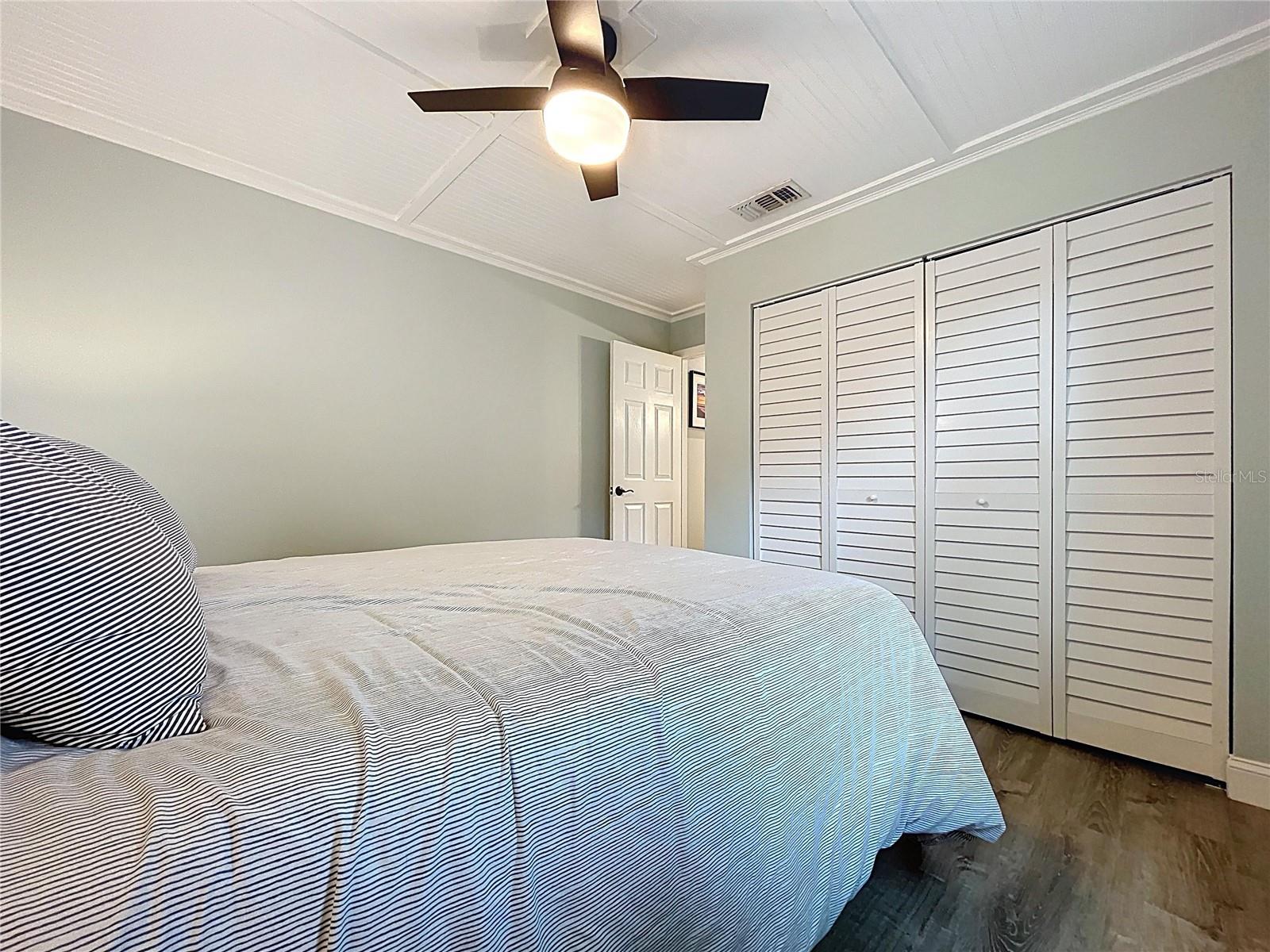 Additional view of this bedroom highlights a full wall of closet space, ceiling fan, and views of tropical landscaping.