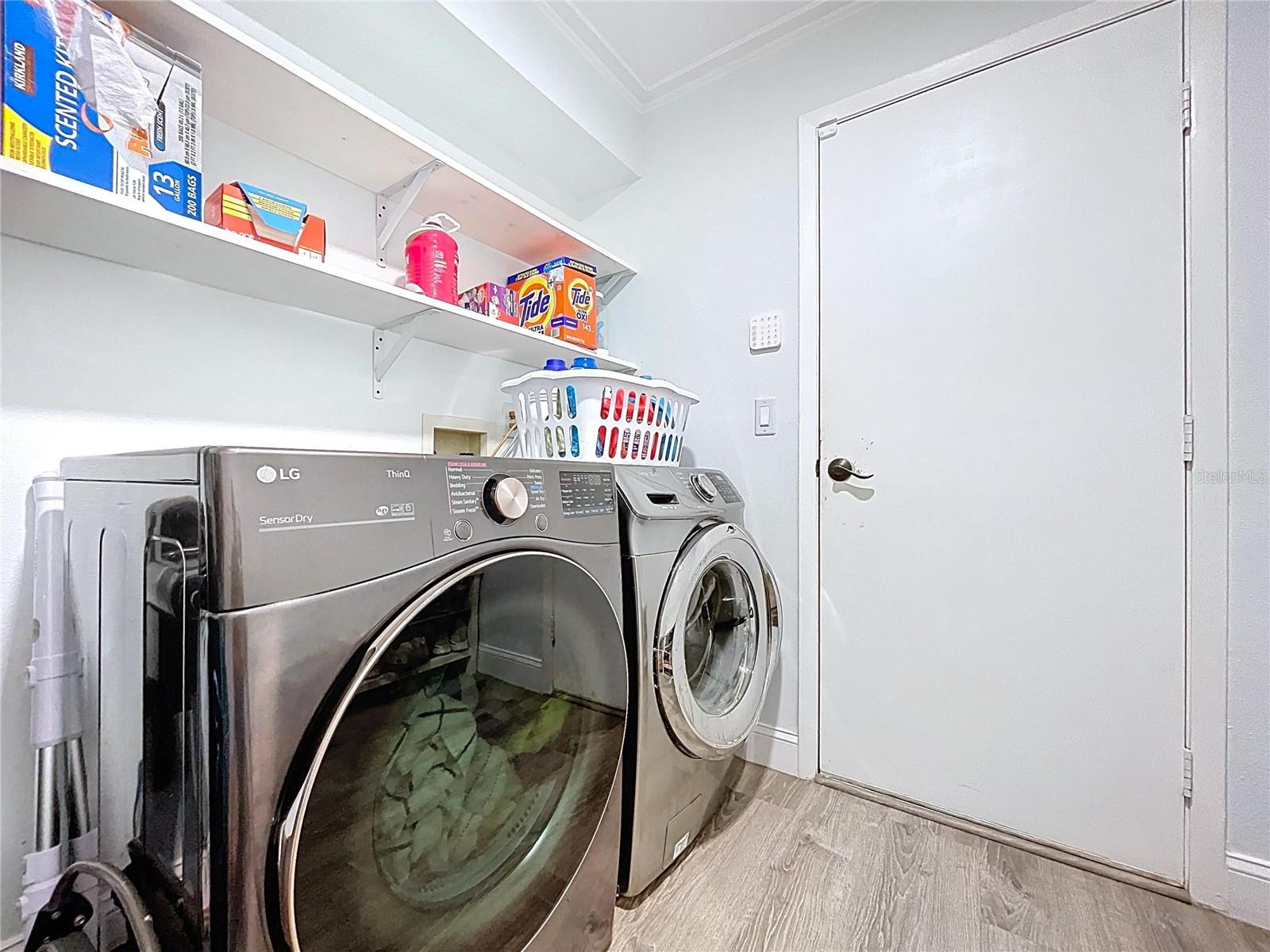 Dedicated laundry room equipped with front-loading washer and dryer, open shelving, and easy garage access.