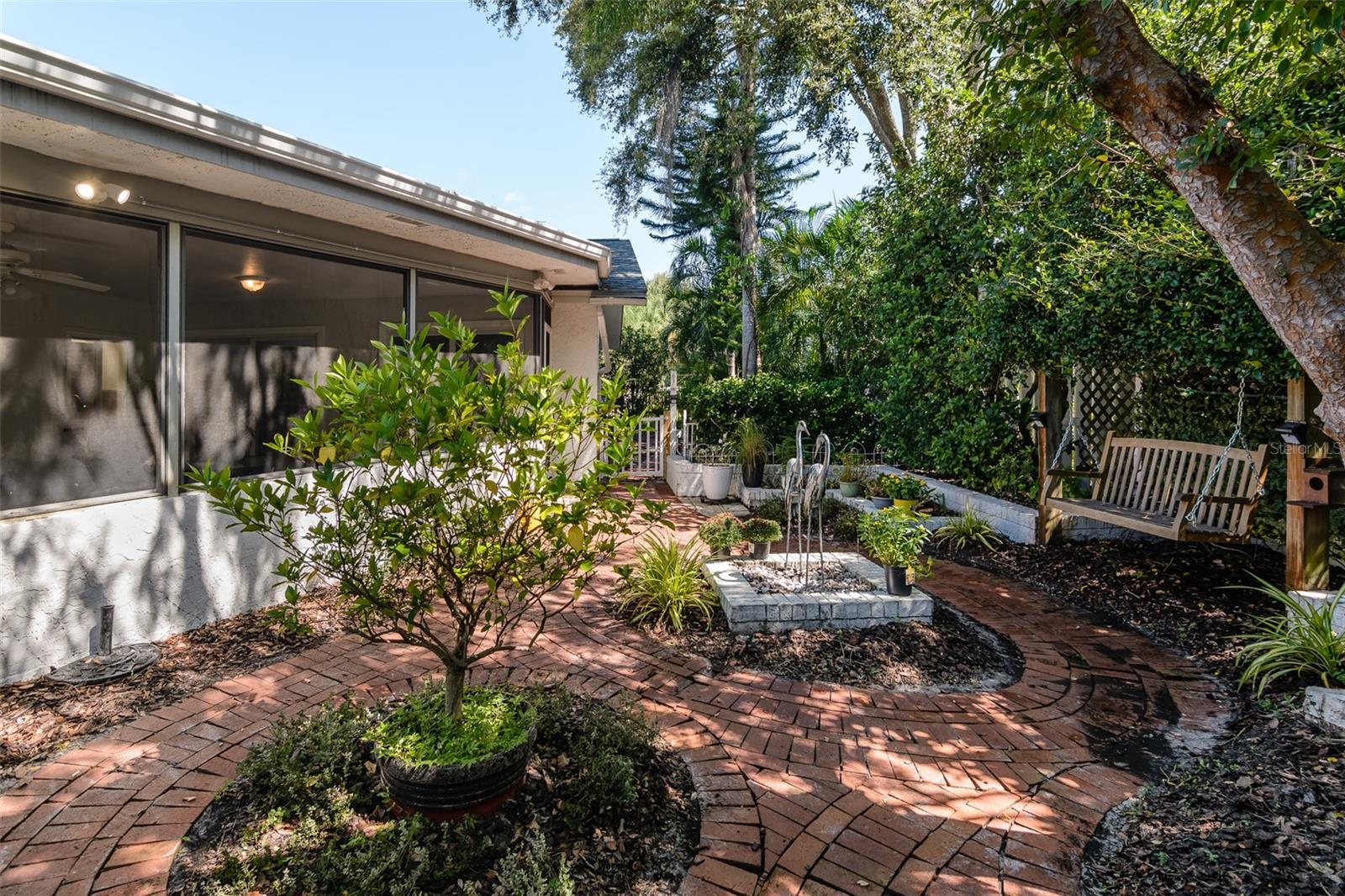 Enchanting courtyard garden with brick pathways and a swing for enjoying a shady, peaceful outdoor space.