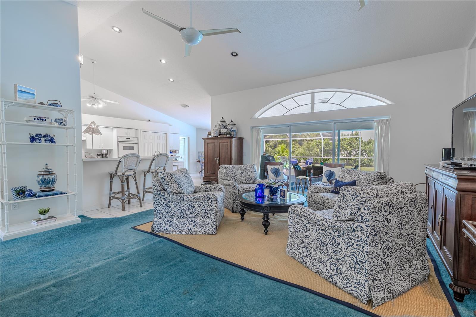 The living room offers vaulted ceilings, abundant natural light, and sliding glass doors leading to the pool area.