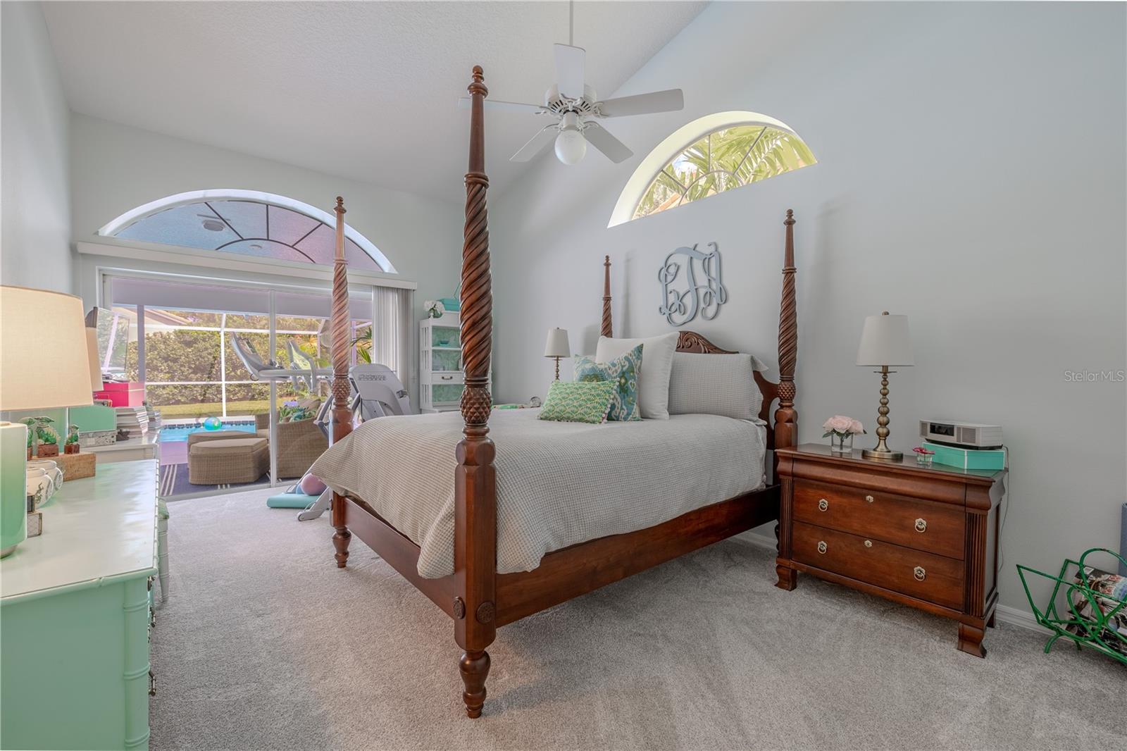 The spacious primary suite features vaulted ceilings, arched windows, and sliding doors that open directly to the pool and lanai for a private retreat.