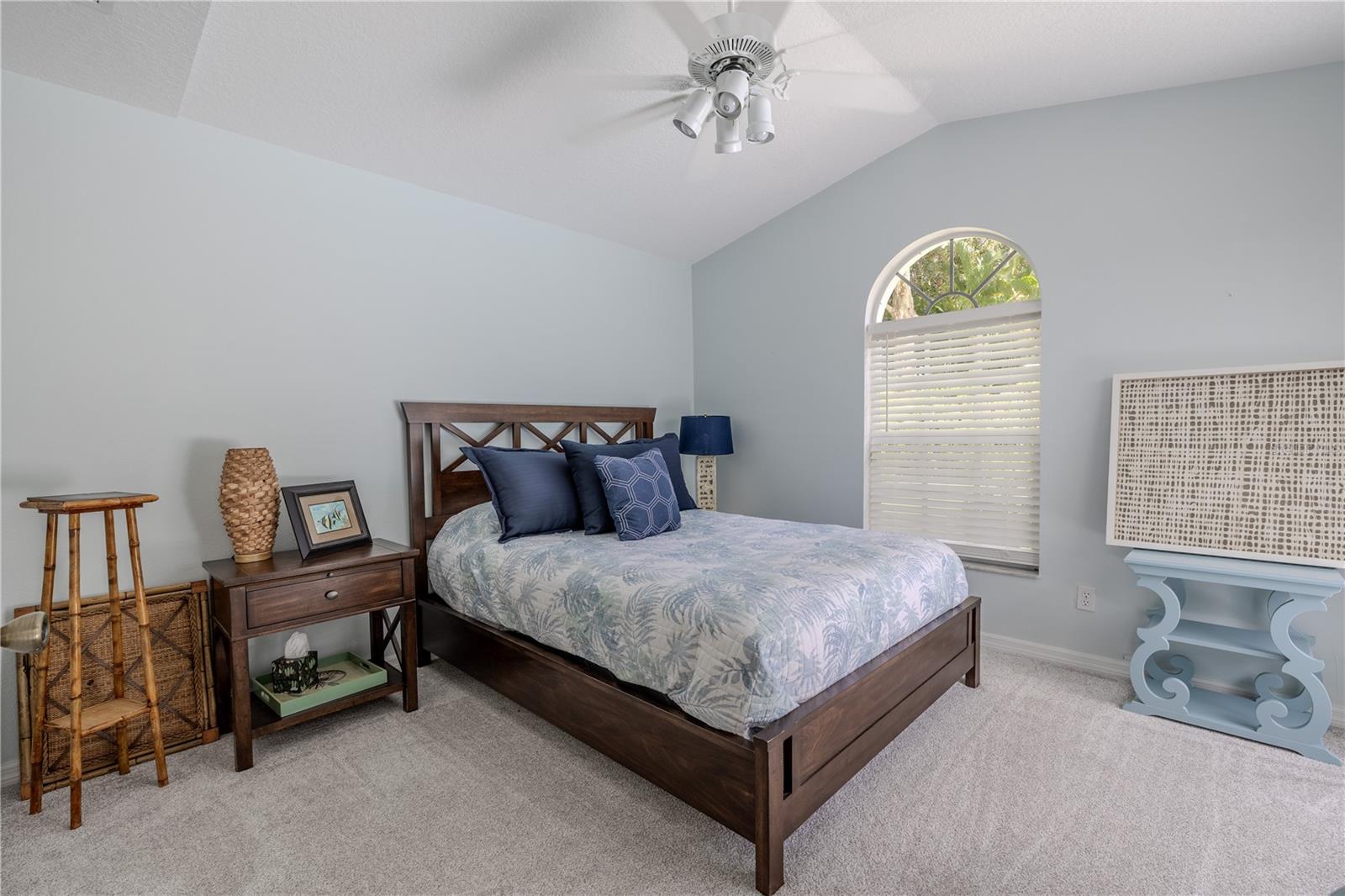 Bedroom two features vaulted ceilings, an arched window, spacious closet, and soft carpet flooring, creating a comfortable retreat for guests or family.