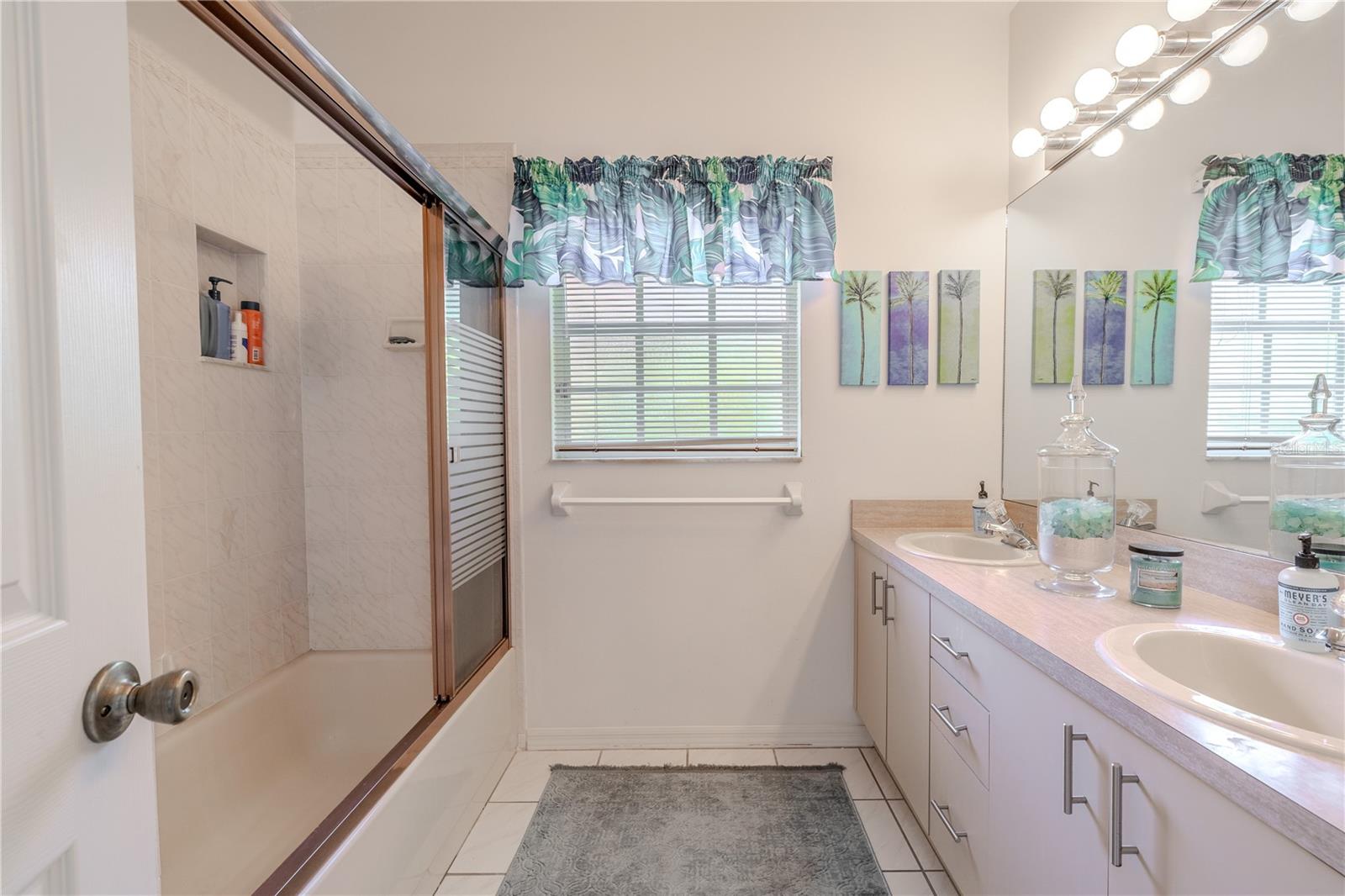 The second full bath features a double vanity with plenty of storage, a tub-shower combination with sliding glass doors, and tile flooring. The toilet is separated by a partial wall for added privacy.