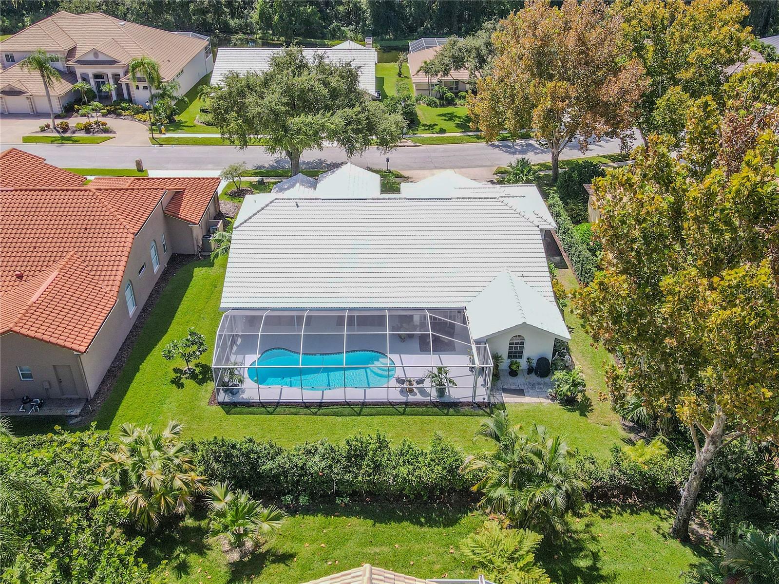 Aerial rear view of the home showcasing the screened-in pool enclosure, spacious backyard, landscaped greenery, and surrounding neighborhood.