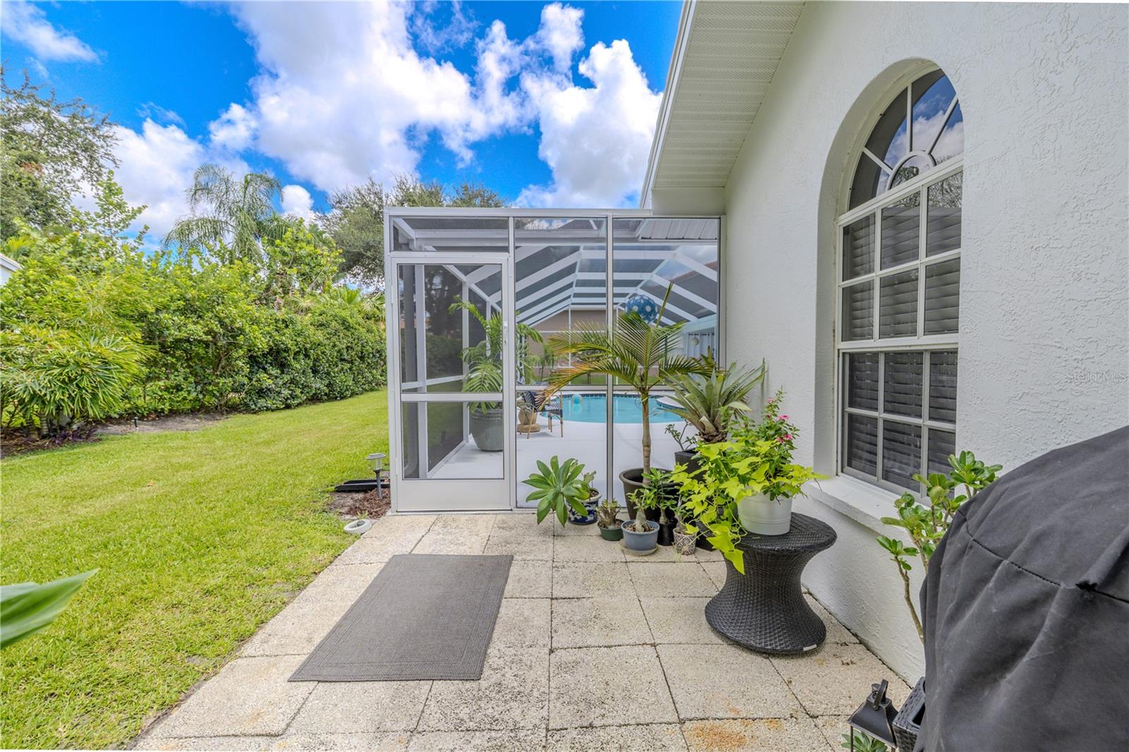 Private side patio leading into the screened pool enclosure, with room for potted plants or a small seating area.