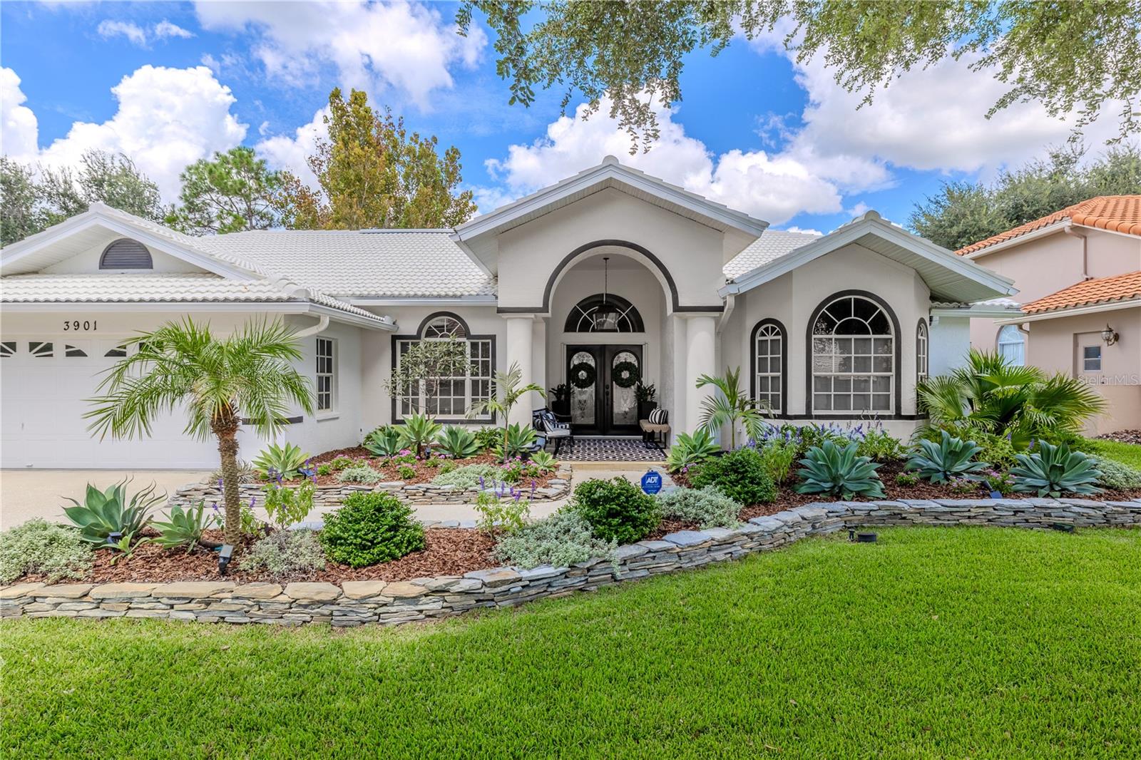 This beautifully landscaped entrance, framed with tropical plants and a grand arched entryway, makes every arrival feel like pulling up to your own private retreat.