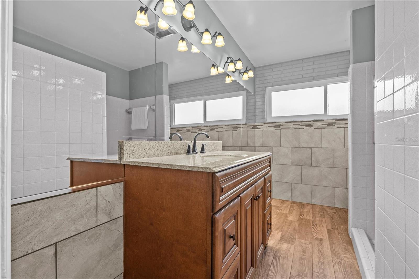 Bathroom 2 with wood-look ceramic tile floor, tile walls and European cabinetry.