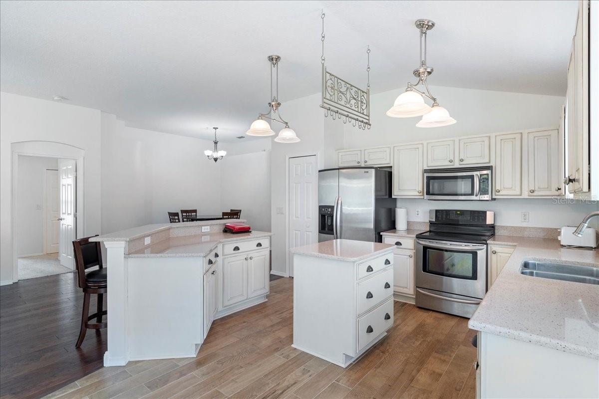 At the center of the home, the light and bright open concept kitchen boasts all wood custom cabinets with pull out drawers, garnet countertops, a breakfast nook in a bay window, nice-sized pantry, center island offering additional prep and storage space, stainless-steel appliances, and a raised breakfast bar countertop overlooking the living room and dining room.