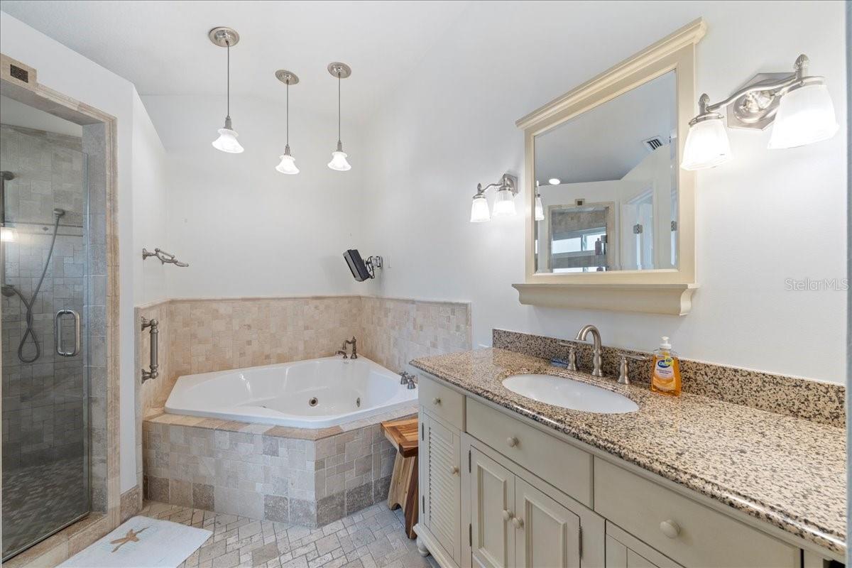 Primary ensuite bathroom featuring a jetted tub, separate Toilet closet, and walk-in shower and spa-like travertine tile accents.