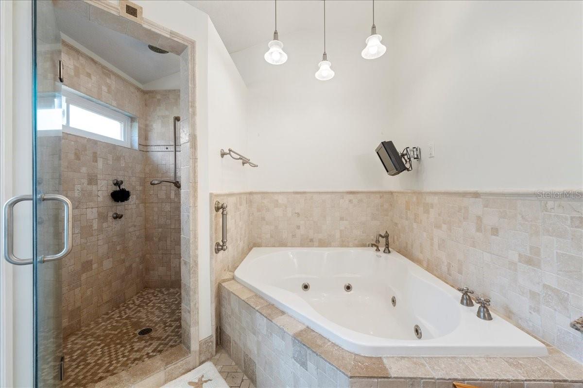 Primary ensuite bathroom featuring a jetted tub, separate Toilet closet, and walk-in shower and spa-like travertine tile accents.