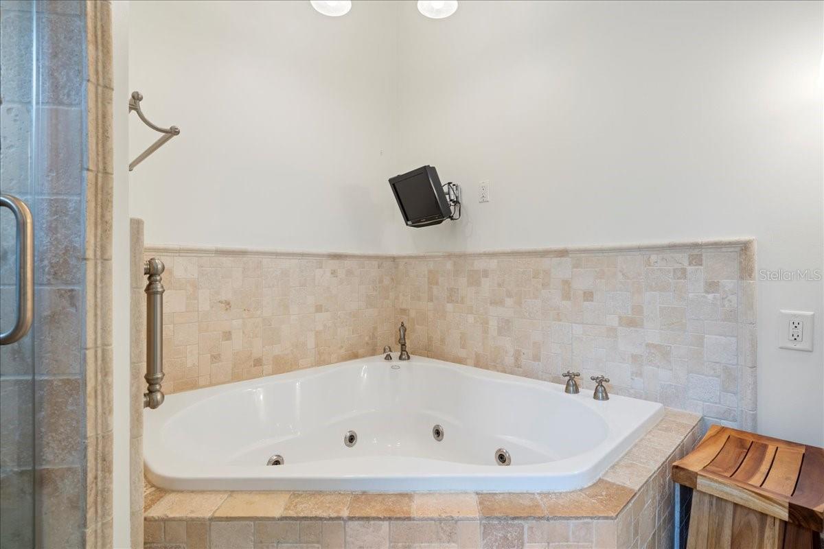 Primary ensuite bathroom featuring a jetted tub, separate Toilet closet, and walk-in shower and spa-like travertine tile accents.