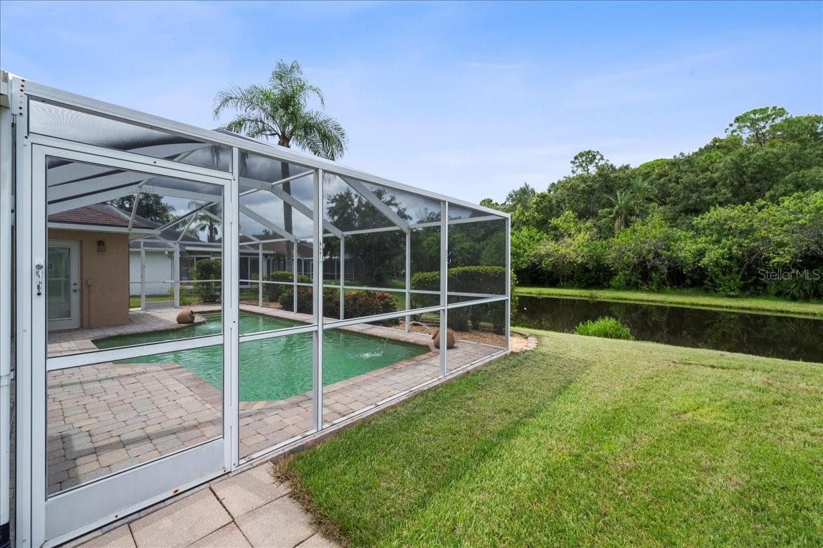 Screened-in pool area with paver deck, water fountain features, sitting shelf and pond view