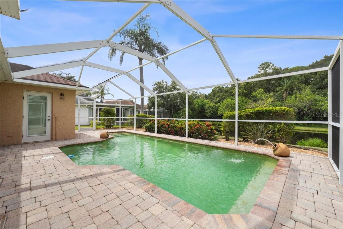 Screened-in pool area with paver deck, water fountain features, sitting shelf and pond view