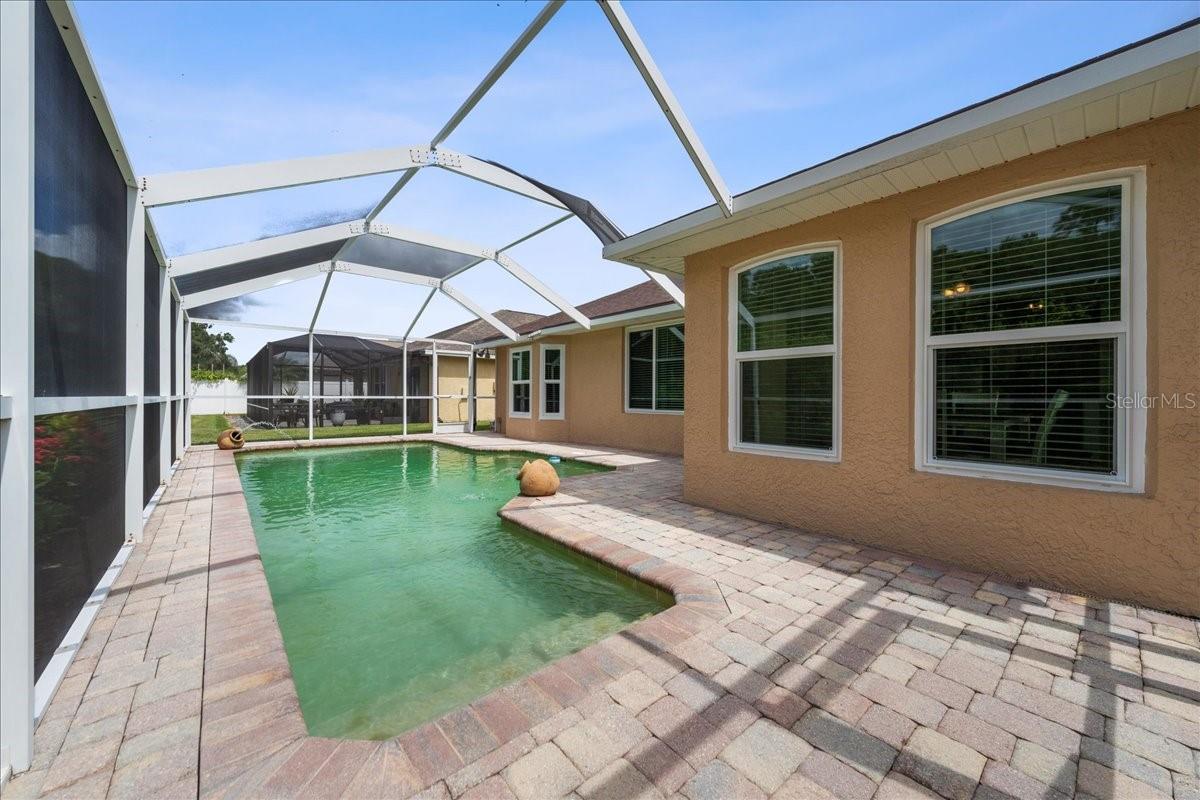 Screened-in pool area with paver deck, water fountain features, sitting shelf and pond view