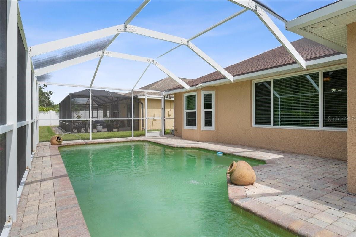 Screened-in pool area with paver deck, water fountain features, sitting shelf and pond view
