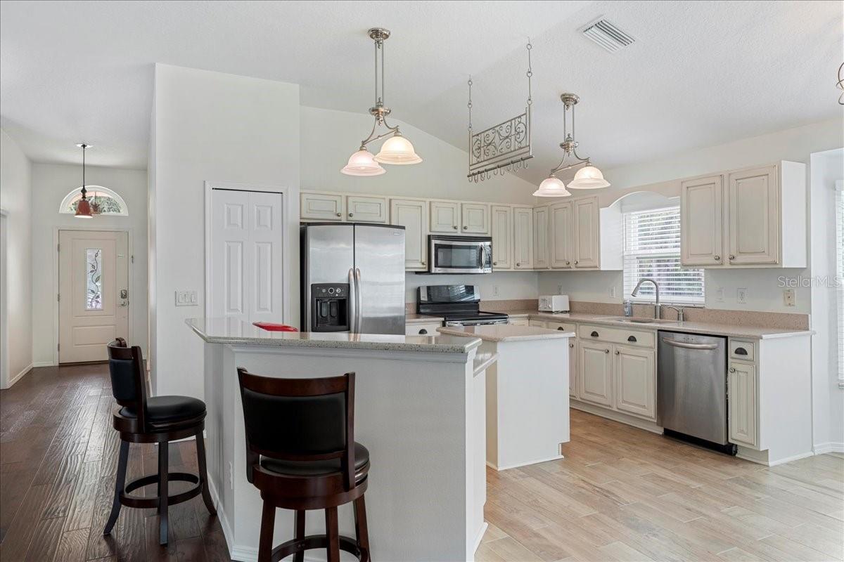 At the center of the home, the light and bright open concept kitchen boasts all wood custom cabinets with pull out drawers, garnet countertops, a breakfast nook in a bay window, nice-sized pantry, center island offering additional prep and storage space, stainless-steel appliances, and a raised breakfast bar countertop overlooking the living room and dining room.