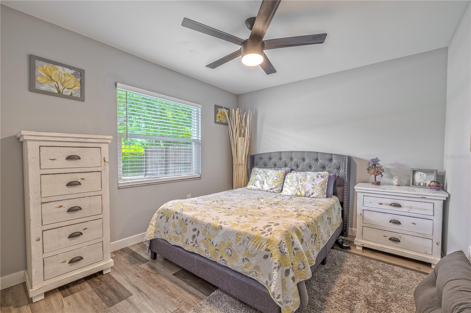 Second bedroom with vinyl plank flooring, ceiling fan with integrated light, and large window providing natural light.