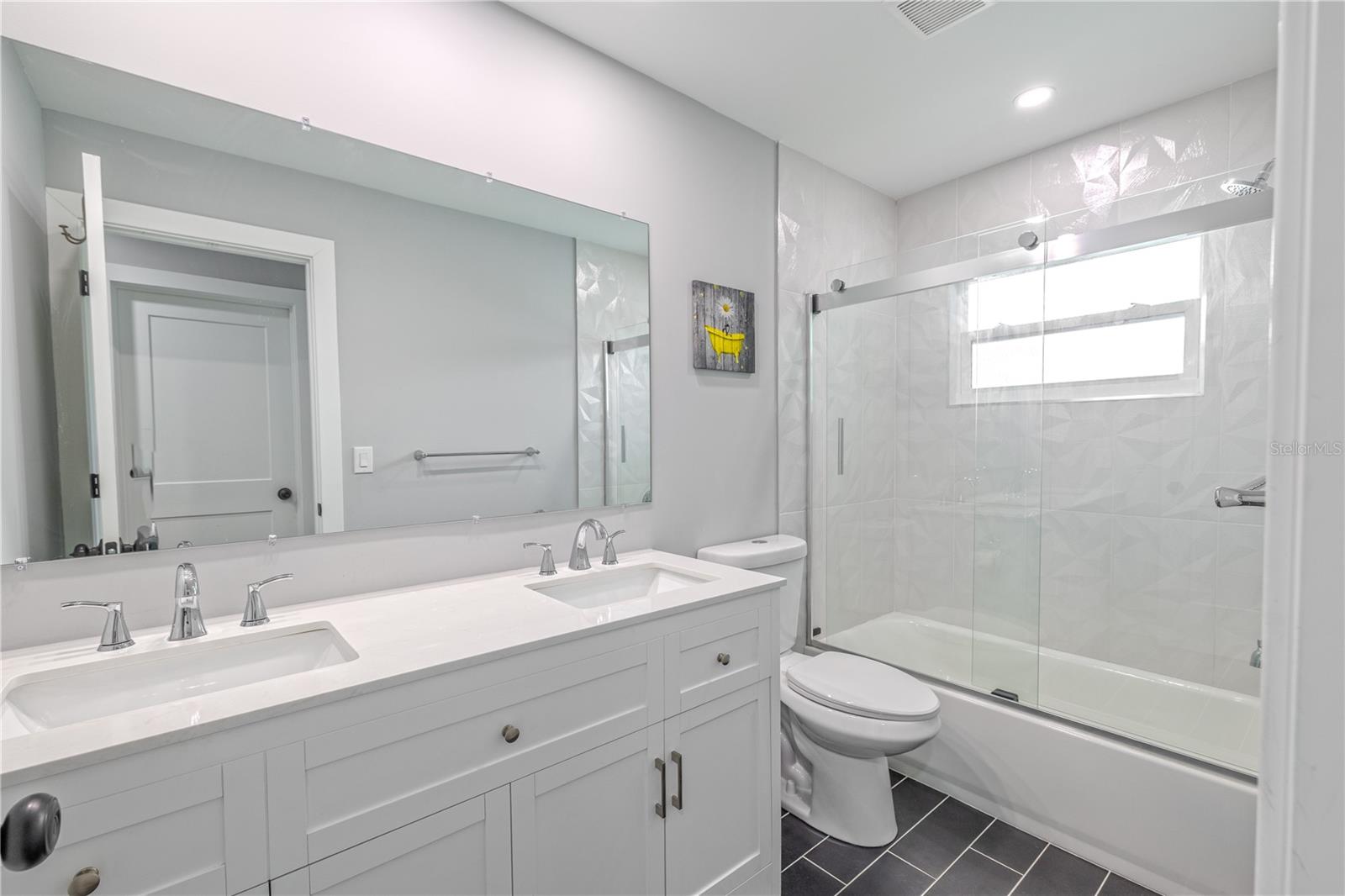 Guest bathroom with dual-sink vanity, large framed mirror, and updated fixtures for everyday convenience.