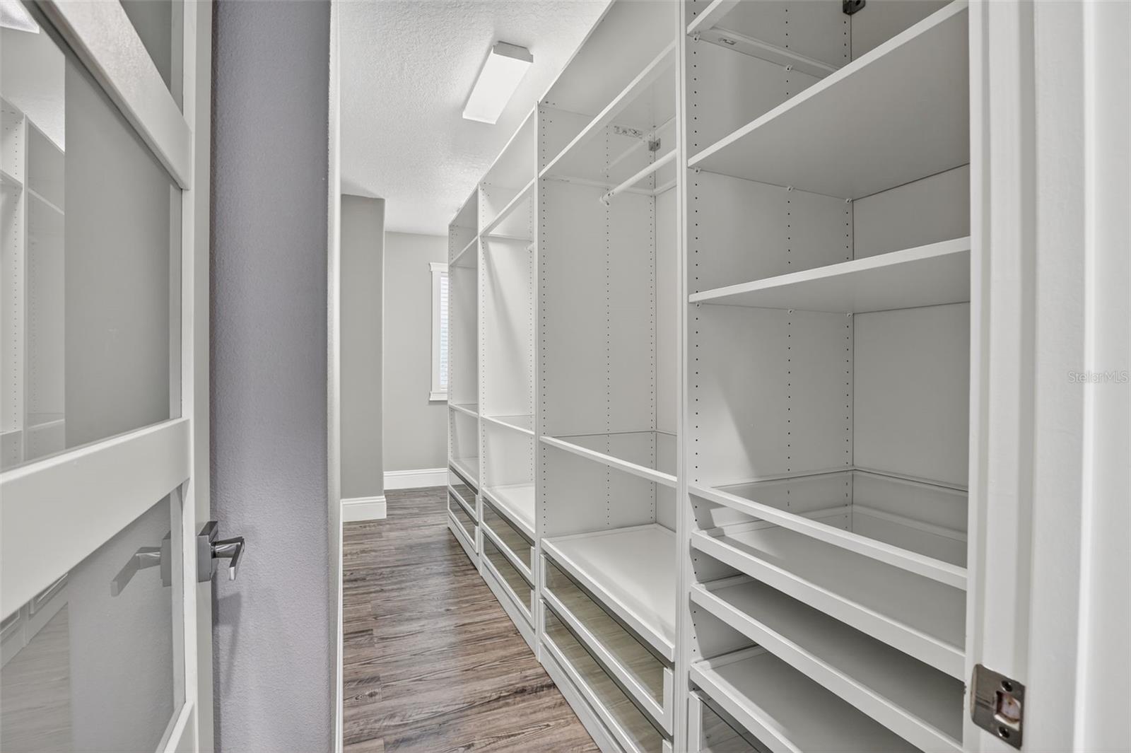 Primary walk-in closet with glass-front drawers & ample shelving and clothes rods.