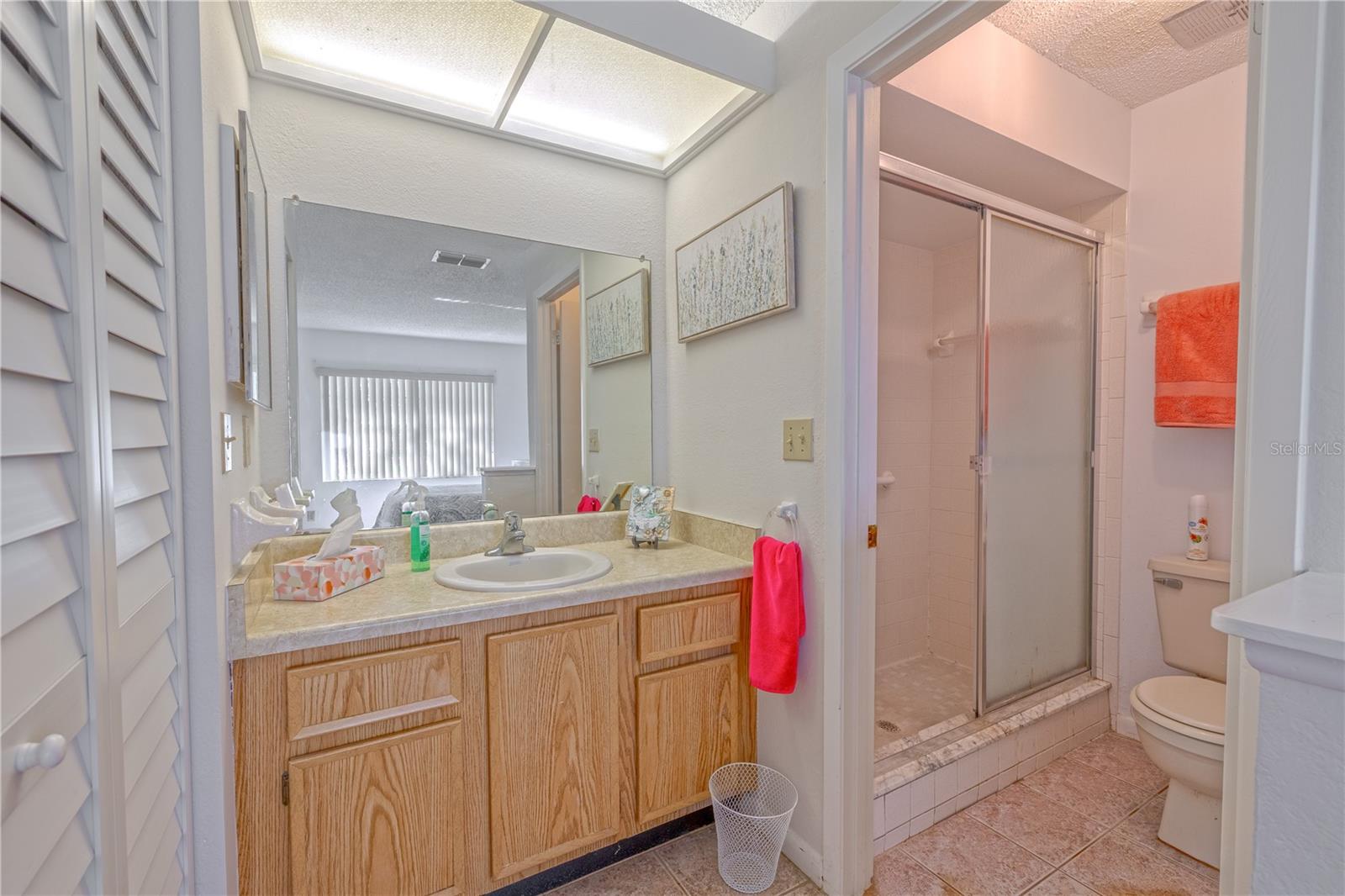 Primary bath with step-in shower, sliding glass doors, and a wide vanity mirror with overhead lighting.