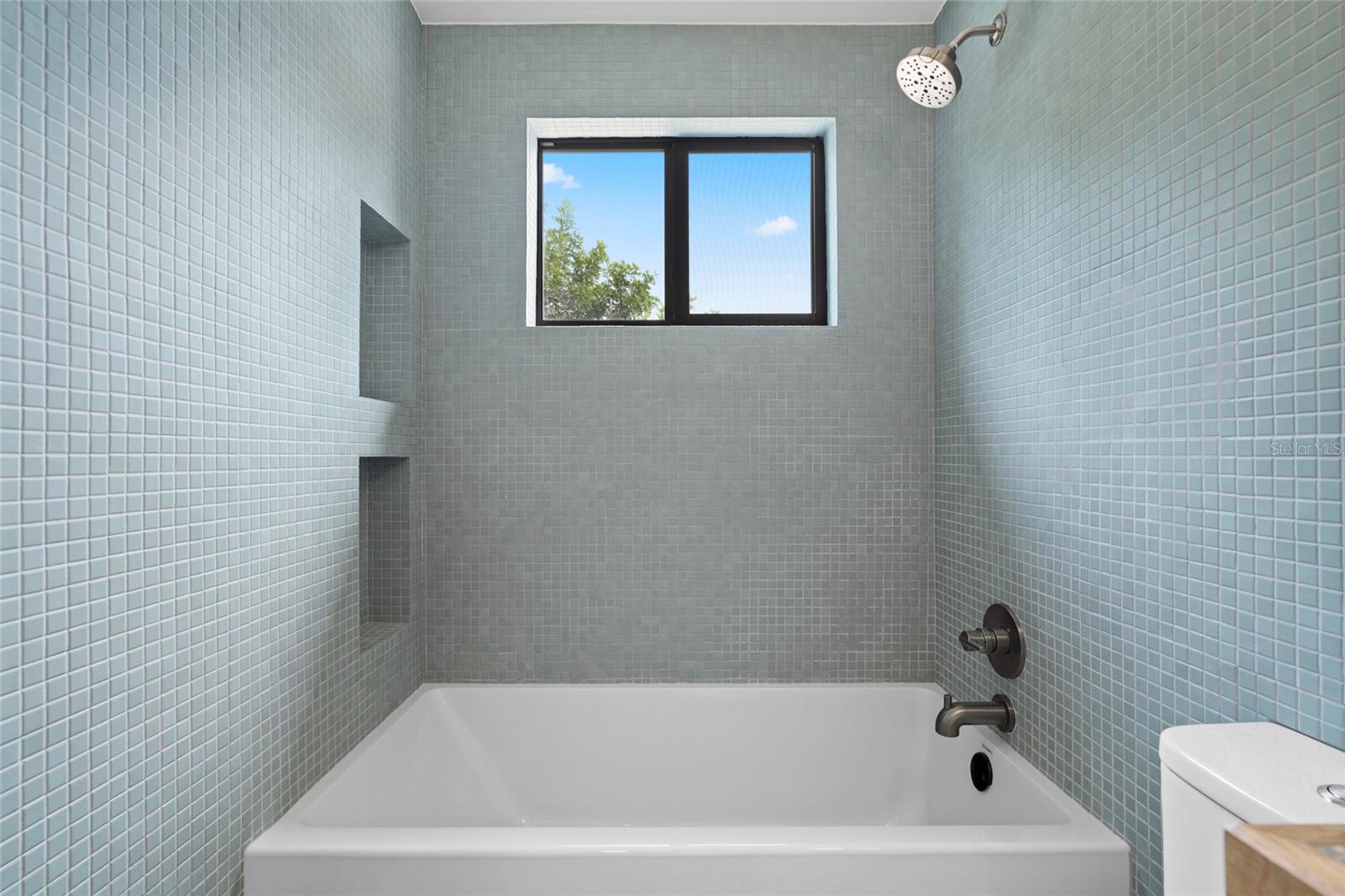 Floor-to-ceiling tiling with built-in shelves and new tub.