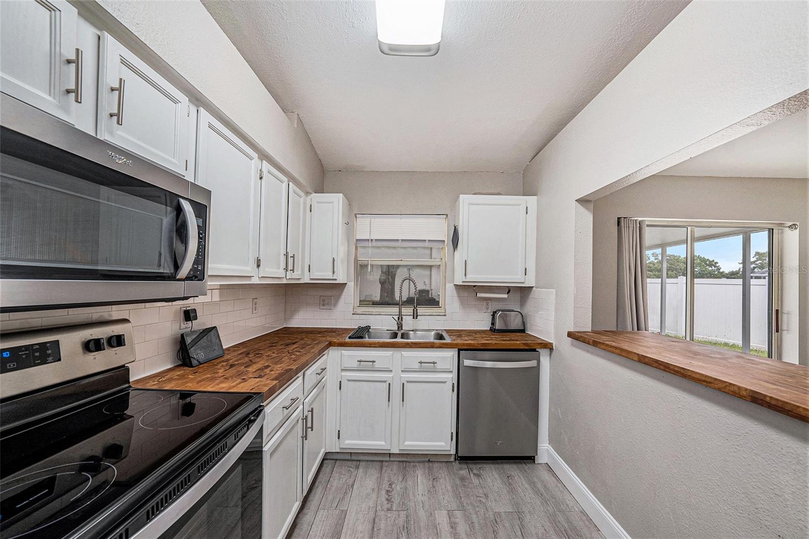 Kitchen window overlooking screened in lanai and large backyard and butcher block breakfast bar.