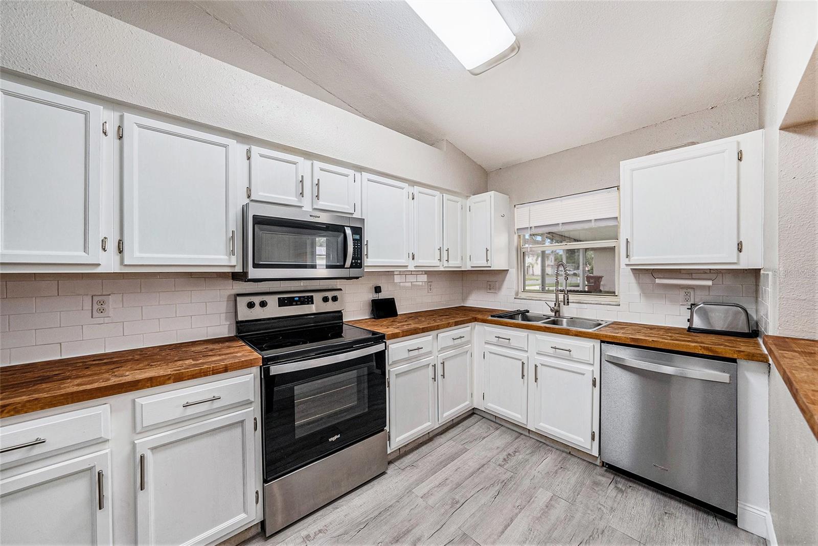Cute and functional kitchen with white wooden cabinets, subway tile backsplash, stainless steel appliances, and butcher block countertops.