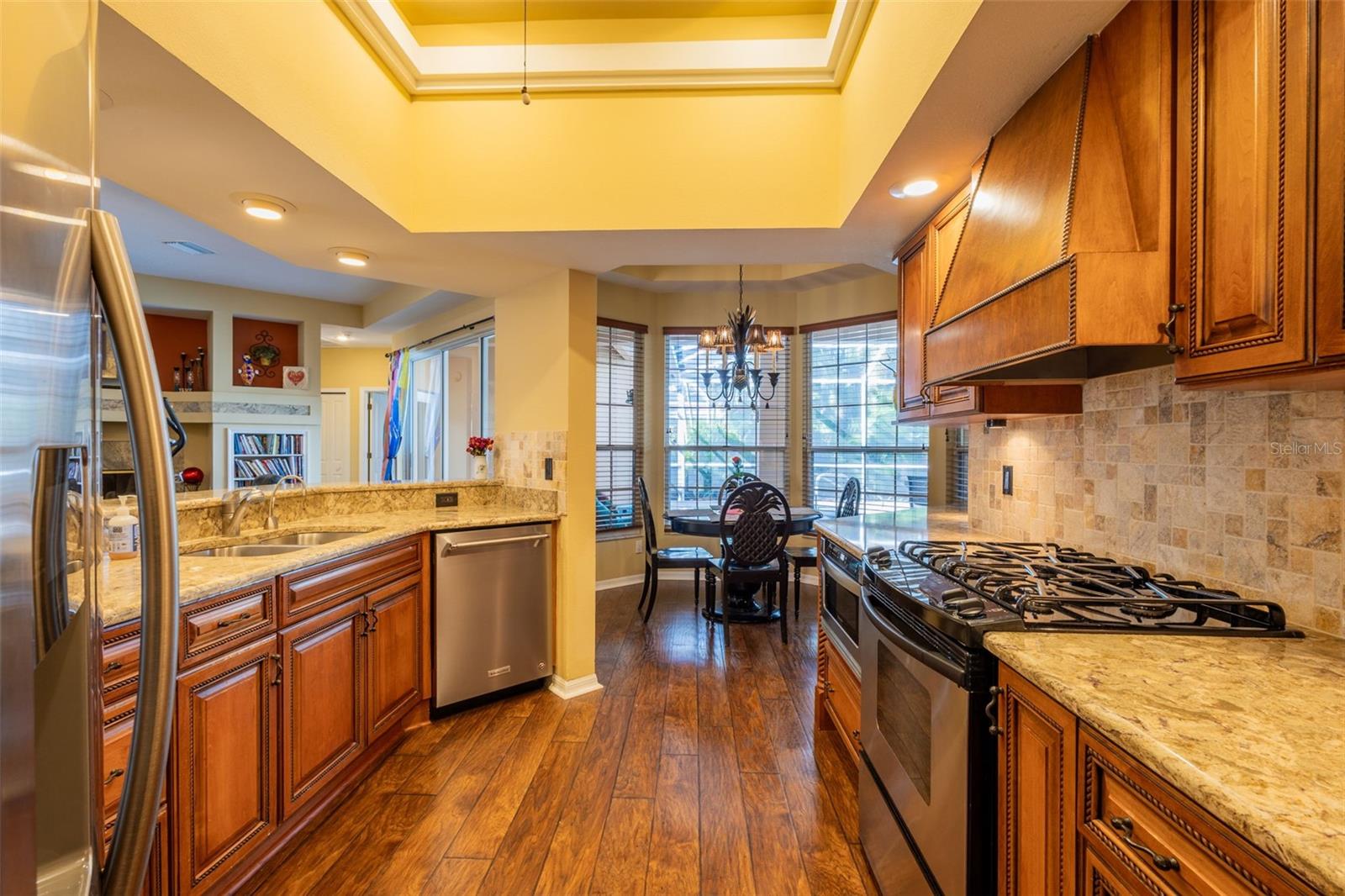 Kitchen with wood cabinetry, stainless appliances (gas stove), breakfast room straight ahead, AND beautiful stone countertops.