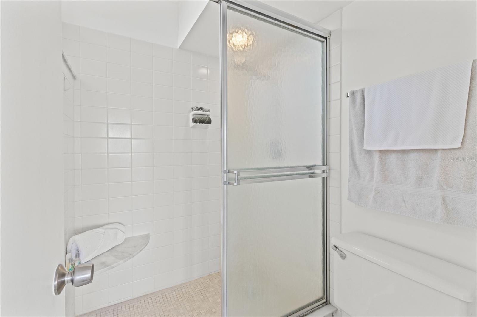 THE TILED SHOWER HAS NEUTRAL COLORED TILES AND A MARBLE SEAT.