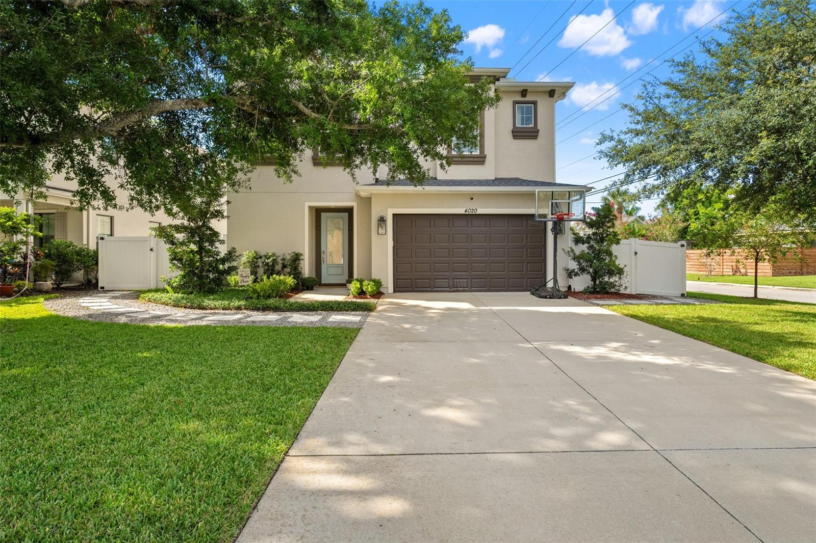 Wide driveway leading to a two-car garage with clean landscaping and mature shade trees.