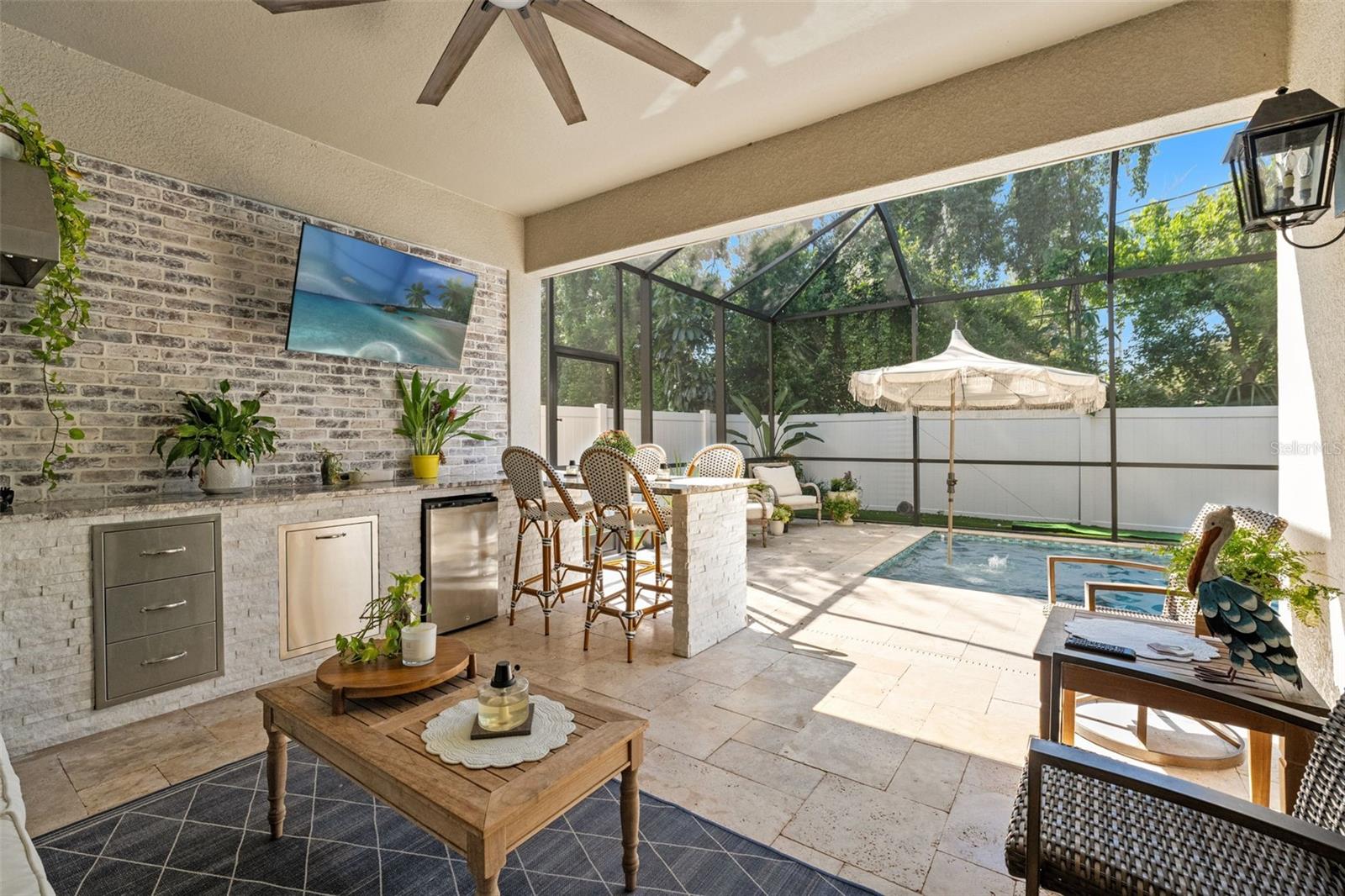Screened-in outdoor living space with a summer kitchen, mounted TV, and stone accents, perfect for entertaining.