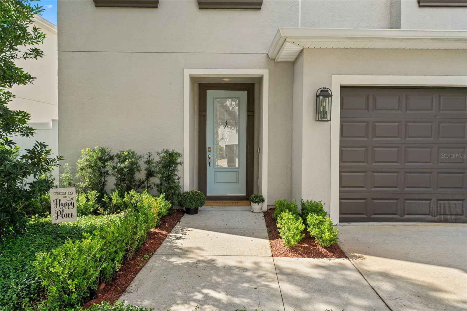 Welcoming entrance with a decorative glass front door, manicured landscaping, and a covered walkway.