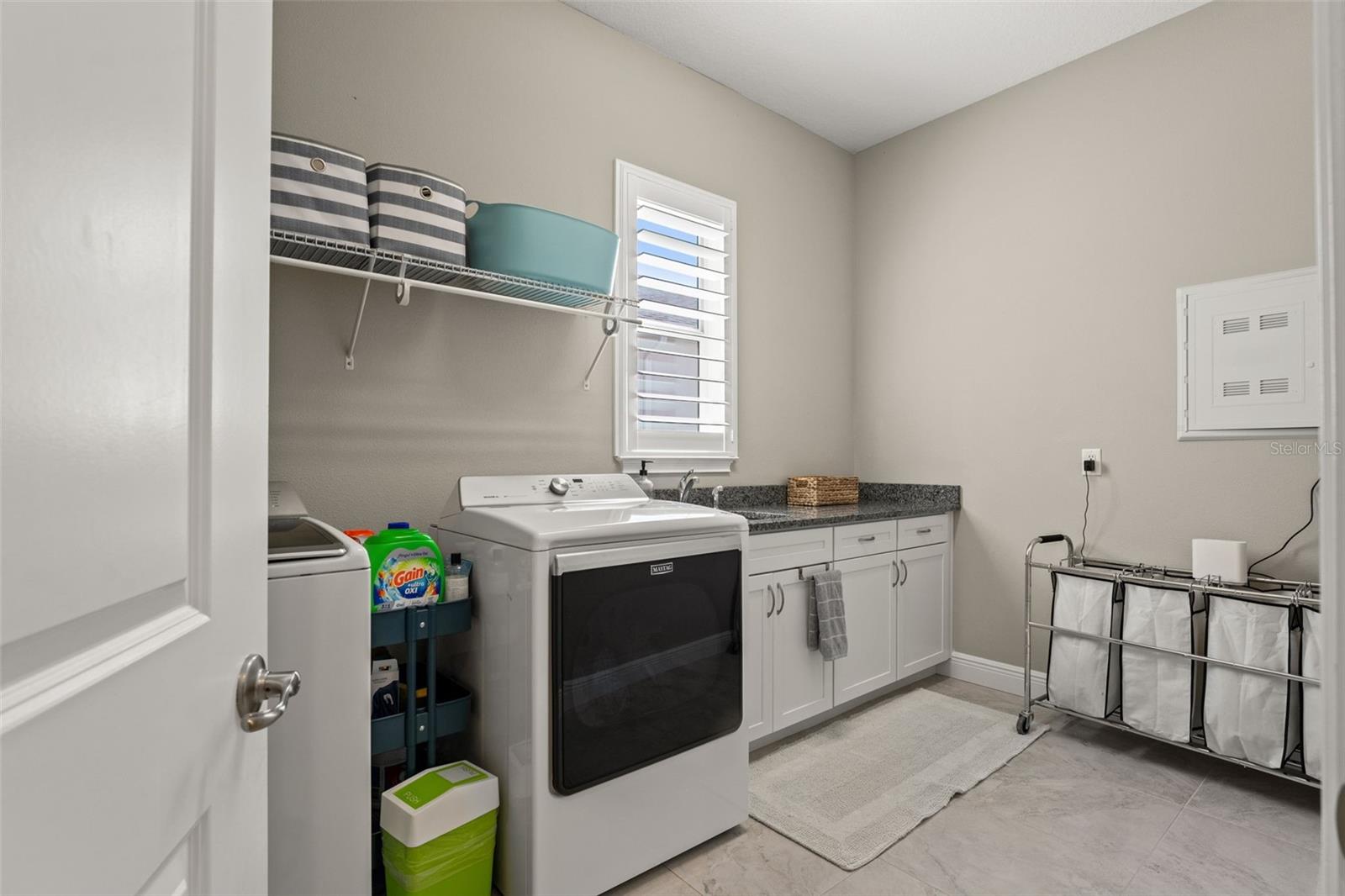 Well-equipped laundry with washer and dryer, granite folding counter, storage cabinetry, and plantation shutter window.