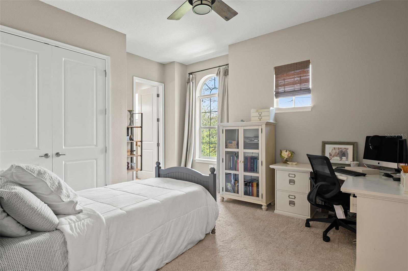Comfortable bedroom with neutral tones, arched window, and flexible layout ideal for rest or study.