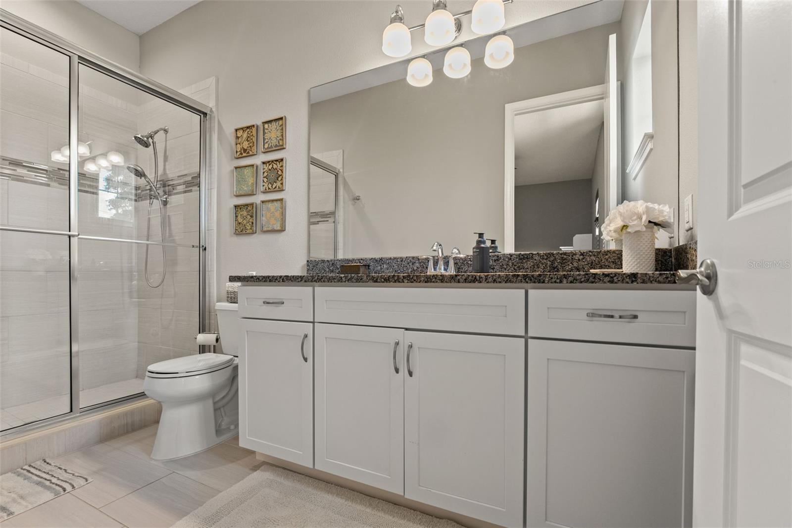 Stylish full bath with granite vanity, framed mirror, and walk-in shower with glass enclosure.