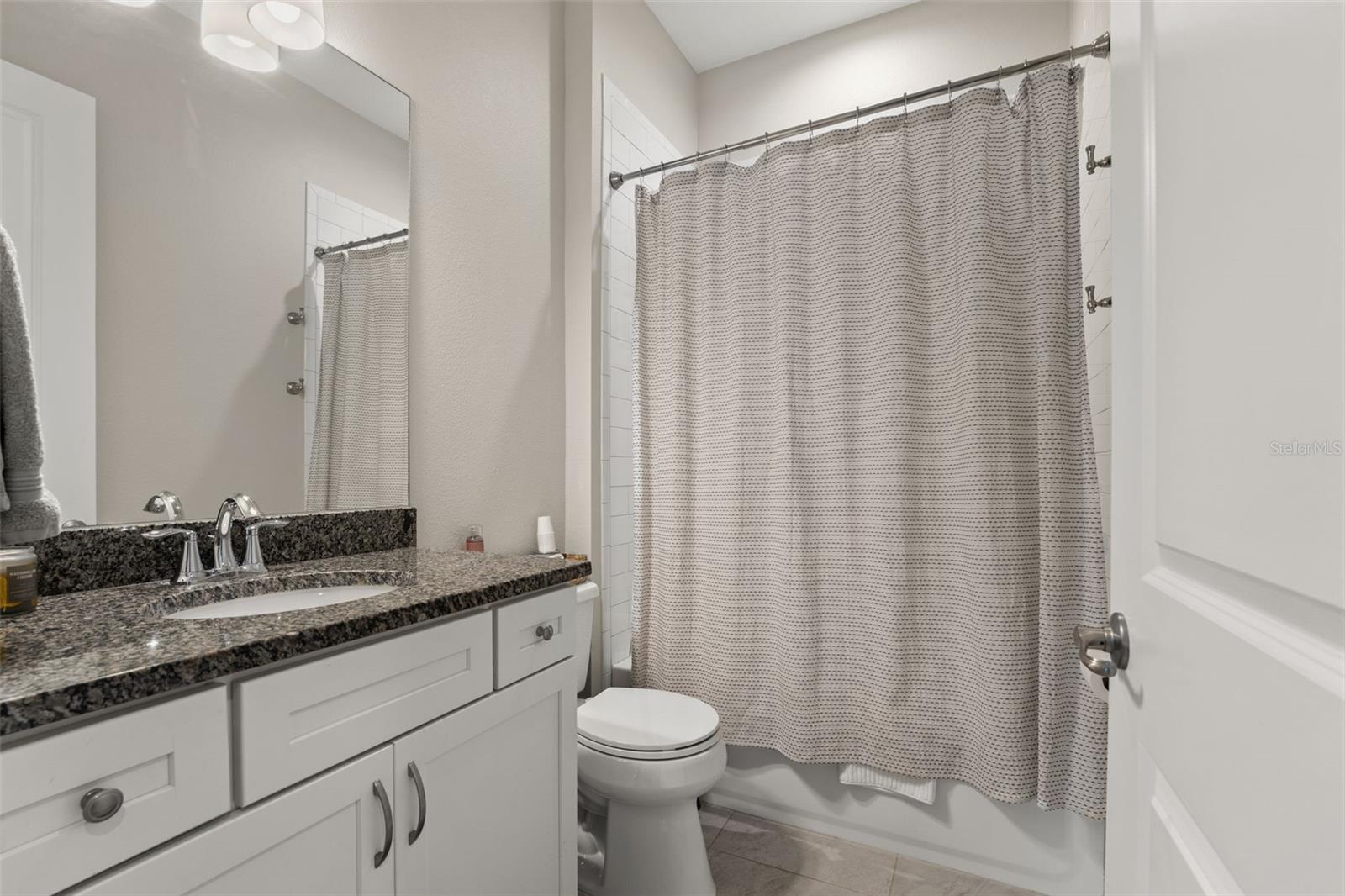 Convenient full bath featuring granite vanity, subway tile tub/shower combo, and modern fixtures.