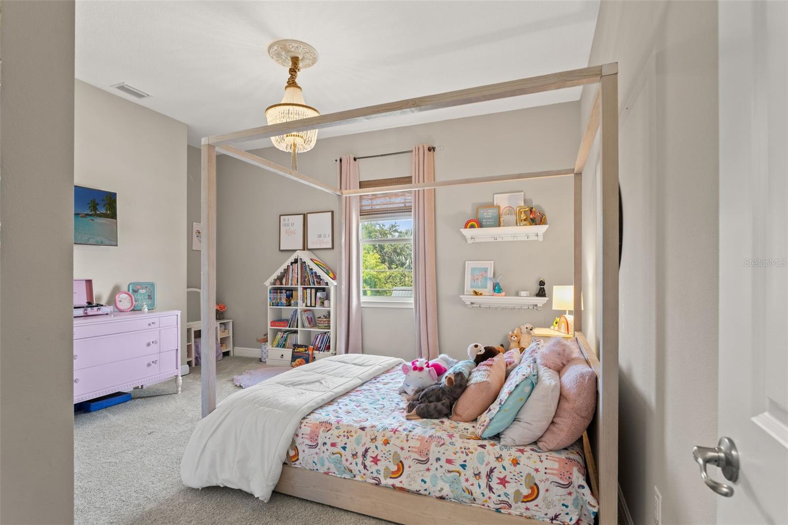 Cheerful bedroom with chandelier lighting, soft neutral walls, and window views, ideal for a nursery or playroom.
