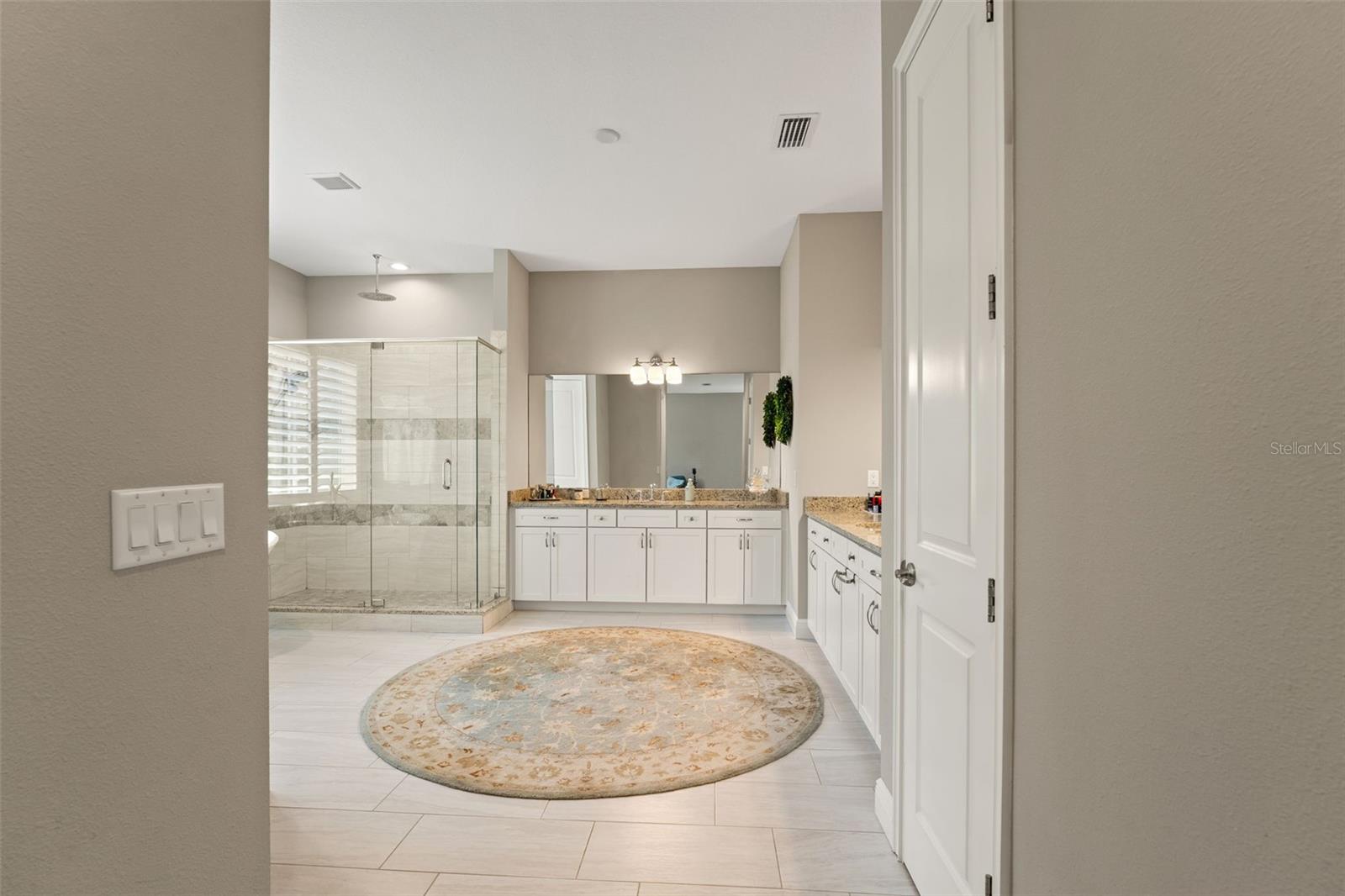 Open layout leading to a luxury bath with granite dual vanities, tile floors, and glass-enclosed shower.