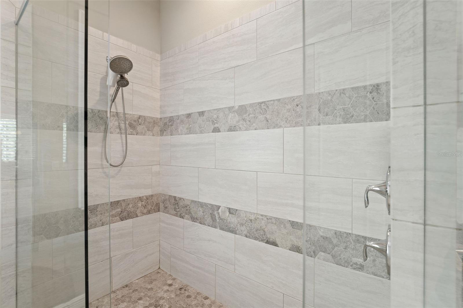 Frameless glass walk-in shower with custom tilework, rain showerhead, and handheld sprayer.