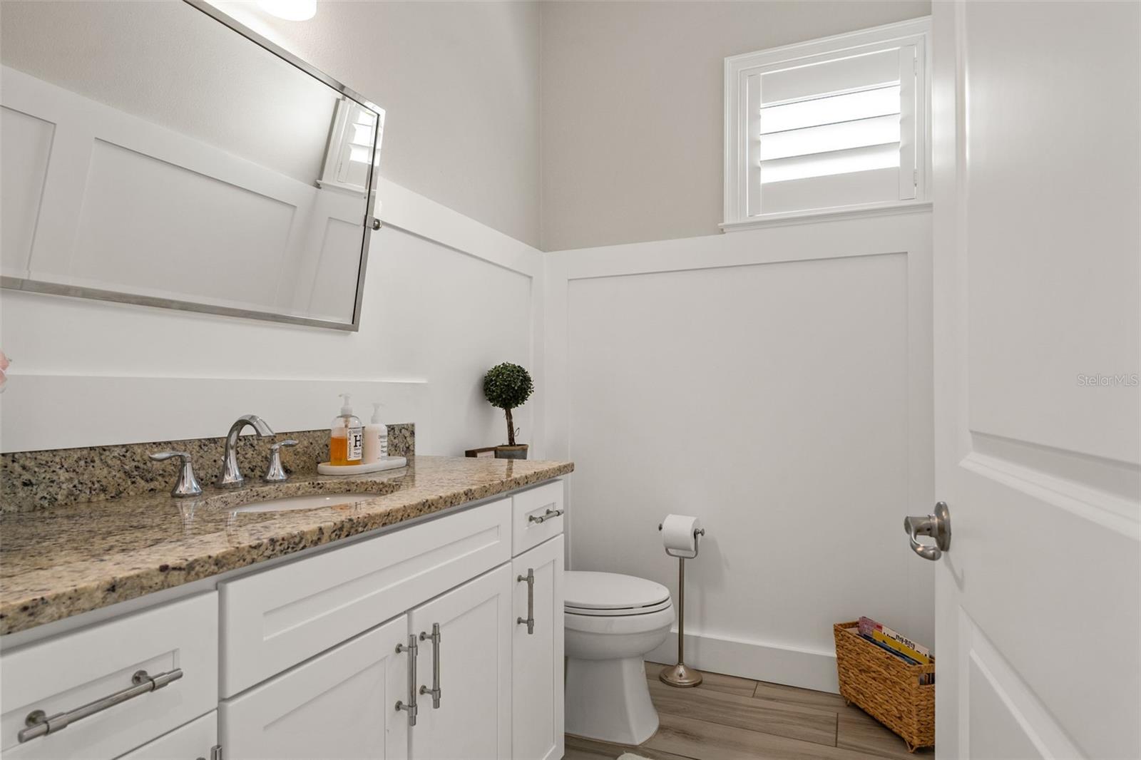 Convenient half bath with granite countertop, white cabinetry, and modern fixtures.