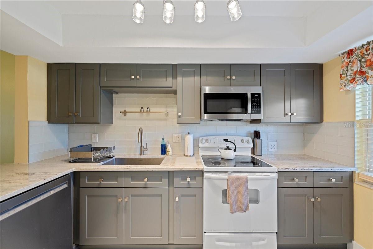 The updated kitchen boasts solid wood shaker-style cabinets, granite countertops, a large farmhouse sink, and a tasteful tile backsplash in clean, modern colors.
