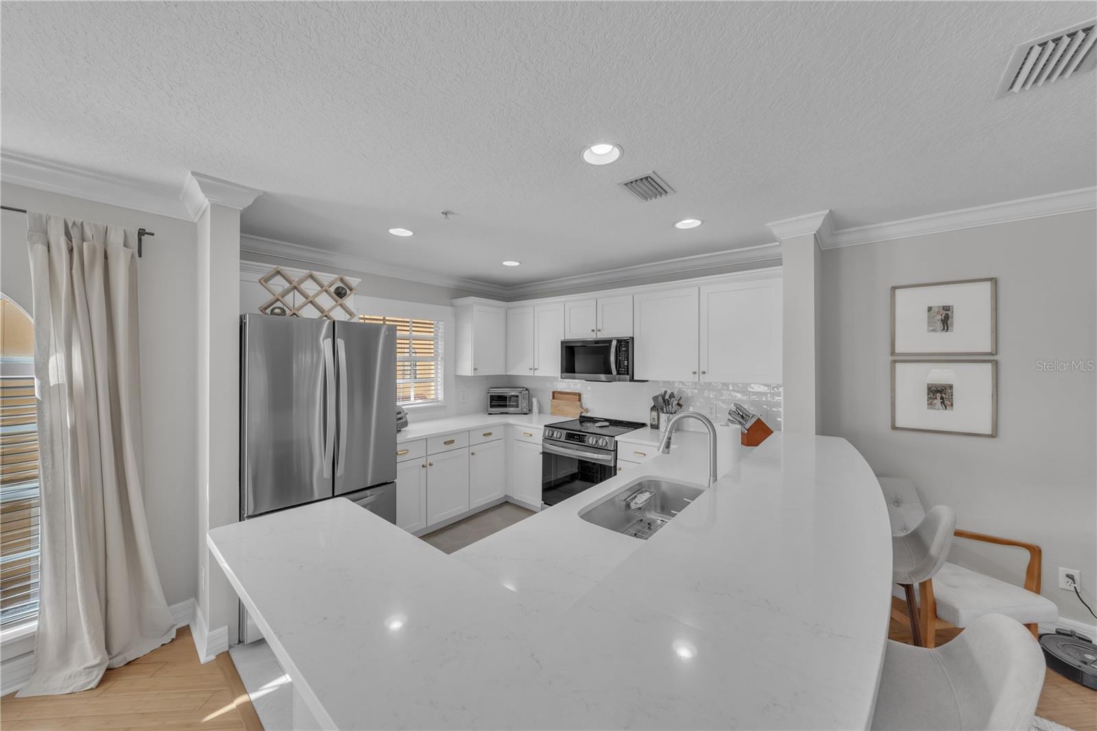 Fully updated kitchen with designer Quartz, Stainless Steel Appliances, breakfast bar seating, white wooden cabinetry, and recessed lighting