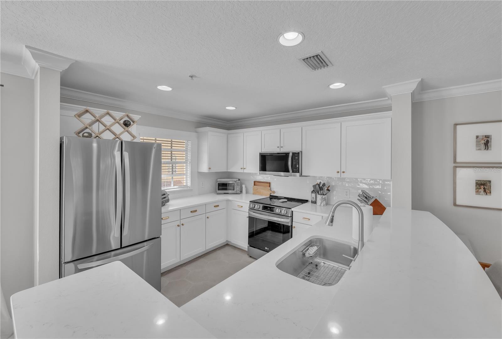Fully updated kitchen with designer Quartz, Stainless Steel Appliances, breakfast bar seating, white wooden cabinetry, and recessed lighting